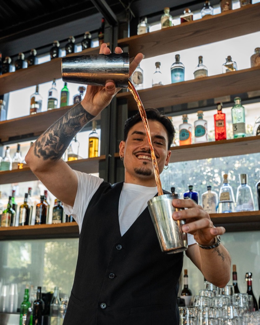 Cris Sola versa un cocktail dallo shaker, dietro il bancone